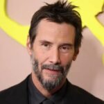 Keanu Reeves smiling on the red carpet at a movie premiere.