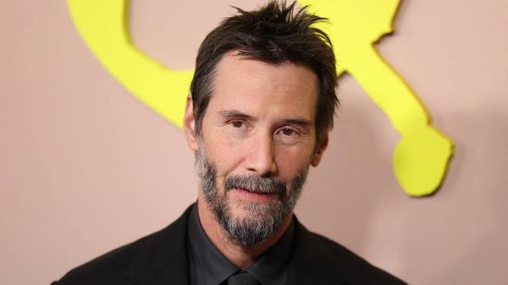 Keanu Reeves smiling on the red carpet at a movie premiere.